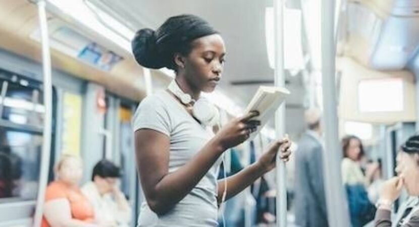 Kvinne leser en bok mens hun står på en buss