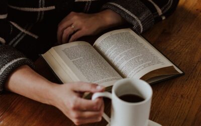 Person leser en åpen bok ved et trebord med en kopp kaffe