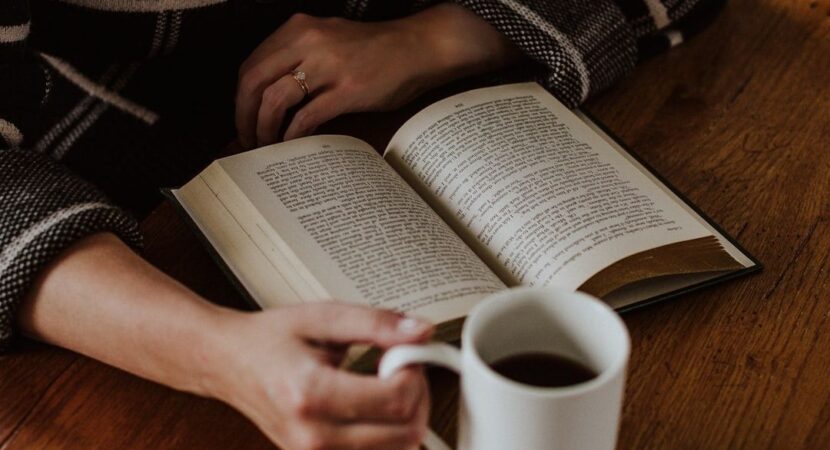Person leser en åpen bok ved et trebord med en kopp kaffe